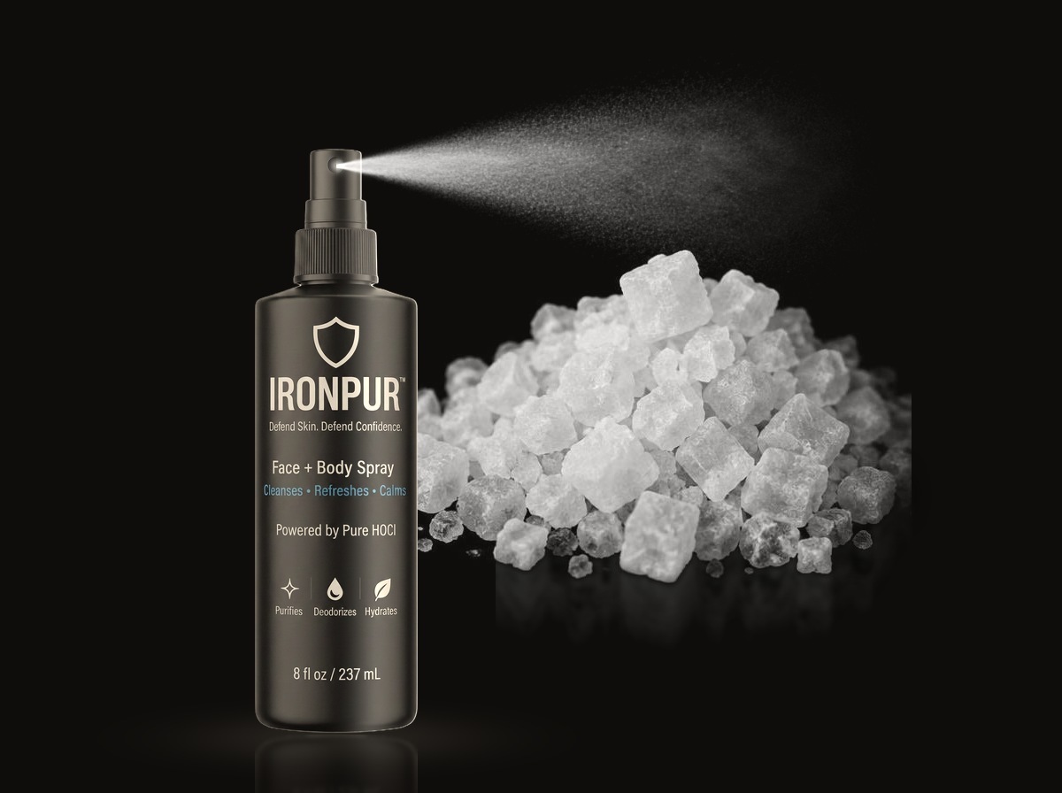 IRONPUR matte black bottle, sprayer uncovered, releasing a fine HOCl mist beside coarse rock salt crystals